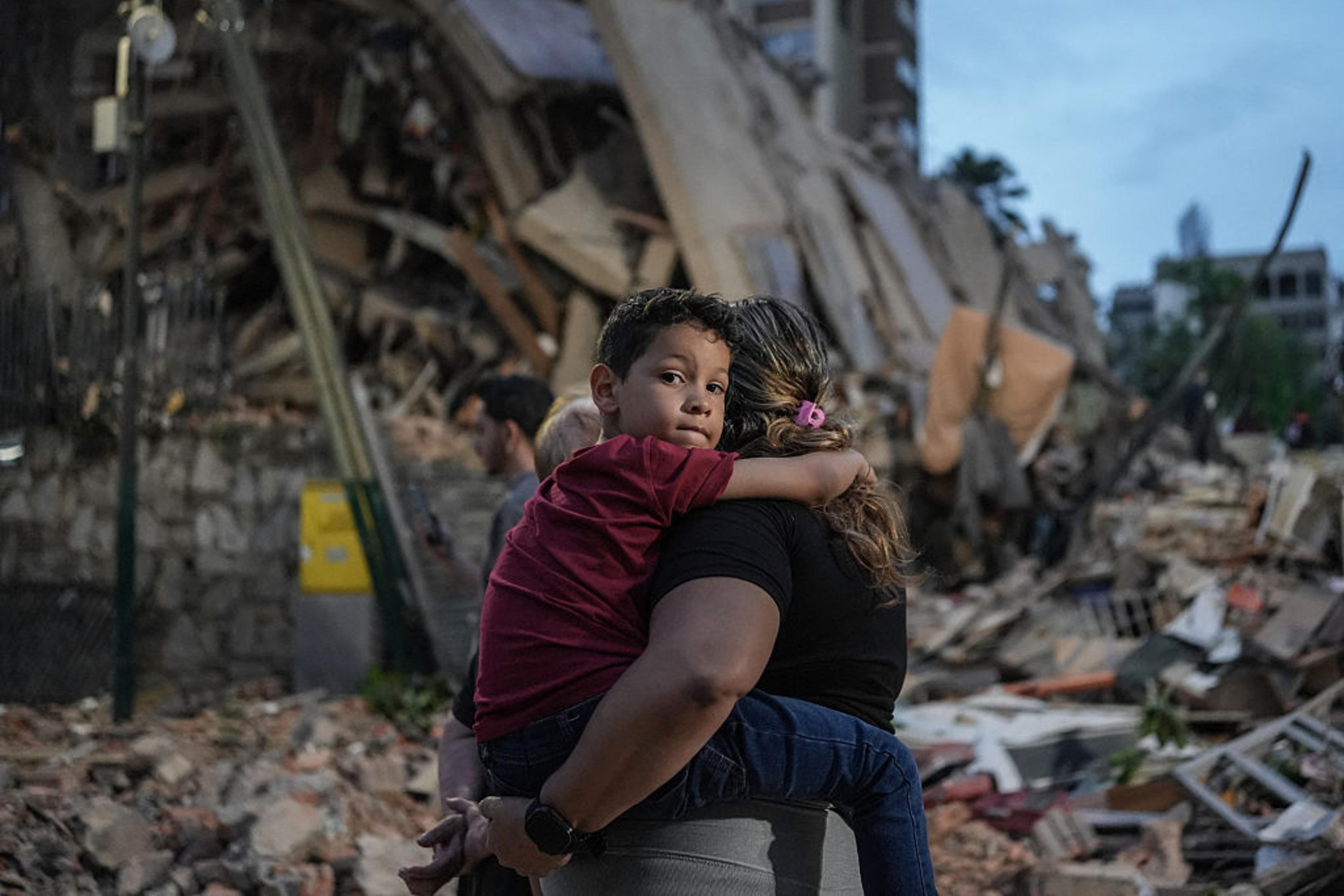 A young child being carried past collapsed buildings after Venezuela’s 2026 earthquake